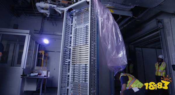 A large, vertically standing, unbranded server rack filled with equipment is being installed by workers in a dimly lit data center.