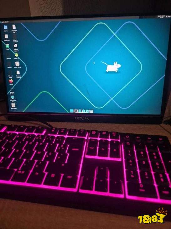 A desktop setup features an ARZOPA monitor displaying a custom Linux desktop interface with a mouse logo and a neon pink backlit keyboard.
