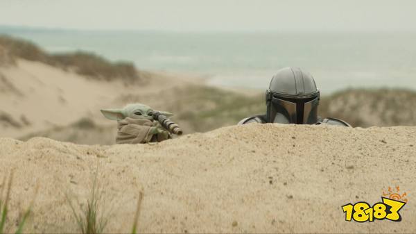 Grogu holds a spyglass while peeking over a sand dune alongside Din Djarin in The Mandalorian and Grogu.