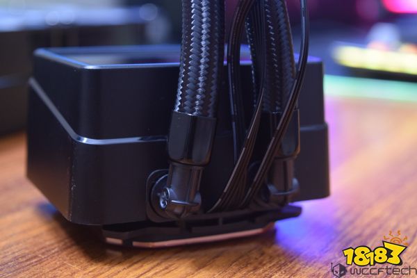 Close-up of an unbranded liquid CPU cooler with a black radiator and braided tubing on a wooden surface.