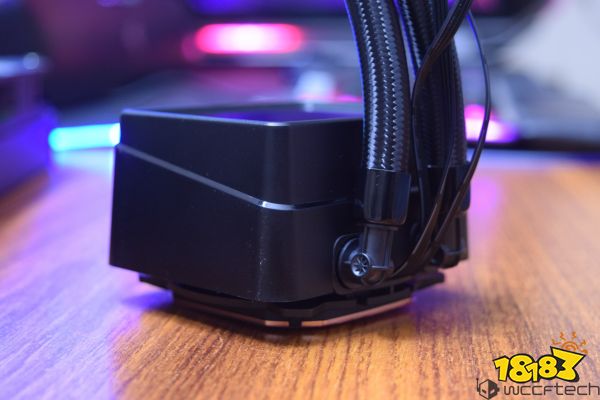 A close-up of a black unbranded liquid CPU cooler on a wooden surface with visible tubing connections.