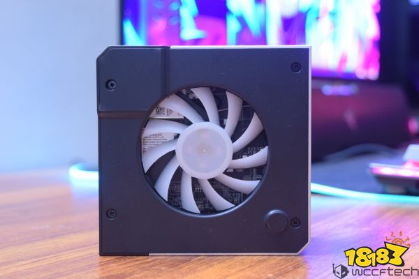 A close-up of a small, unbranded cooling fan unit on a wooden surface with a colorful monitor background.